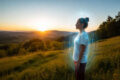 Woman standing in nature surrounded by a visible human energy field during a peaceful meditation at sunset.